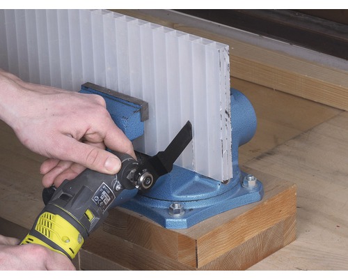 Priehľadná komôrková doska je upnutá v zveráku a je rezaná multifunkčným nástrojom.