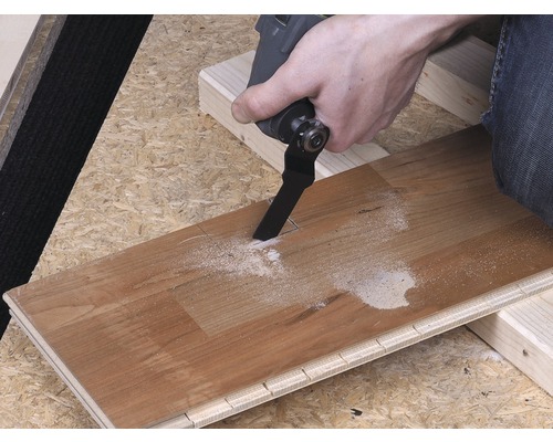 Osoba reže drevenú dosku pomocou multifunkčného nástroja.