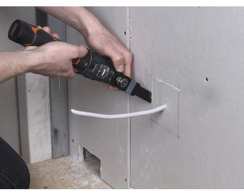 Osoba vyrezáva otvor multifunkčným nástrojom do sadrokartónovej steny pre kábel.