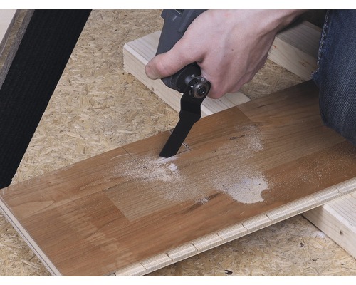 Osoba reže otvor do drevenej dosky pomocou multifunkčného nástroja.