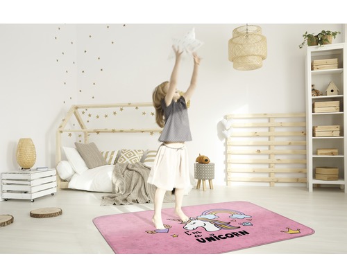Dievča skáče na obdĺžnikovom ružovom koberci s motívom jednorožca v detskej izbe.