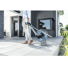 Záhradná scéna s osobou ťahajúcou vozík na hadice so záhradnou hadicou.