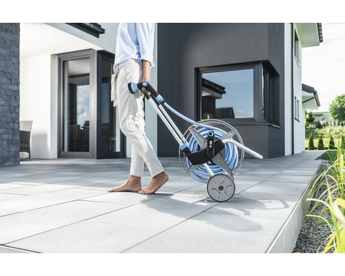 Záhradná scéna s osobou ťahajúcou vozík na hadice so záhradnou hadicou.