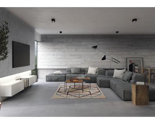 Moderná obývacia izba so sivou rohovou sedačkou, kobercom s geometrickým vzorom a sivými obkladovými dlaždicami.