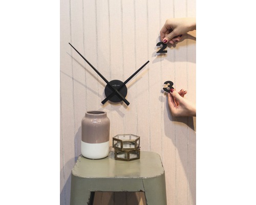 Nástenné hodiny s ručičkami a číslicami na nalepenie, váza a dekoratívne sklenené nádoby na stoličke.