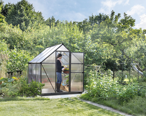 Skleník s otvorenými dverami a osobou starajúcou sa o rastlinu v záhrade