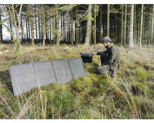 Muž sedí v lese a obsluhuje solárny modul na nabíjanie generátora