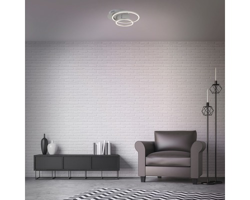 Obývacia izba so stropným svietidlom, kreslom a komodou pred tehlovou stenou.