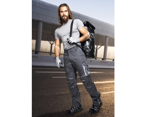 Muž v pracovných nohaviciach s bočnými vreckami, pracovných rukaviciach a pracovnej obuvi nesie tašku cez rameno