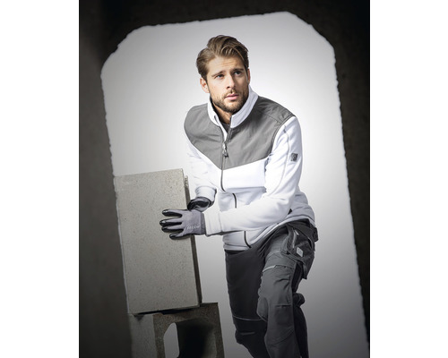 Muž má na sebe pracovný odev a rukavice a drží tehlu