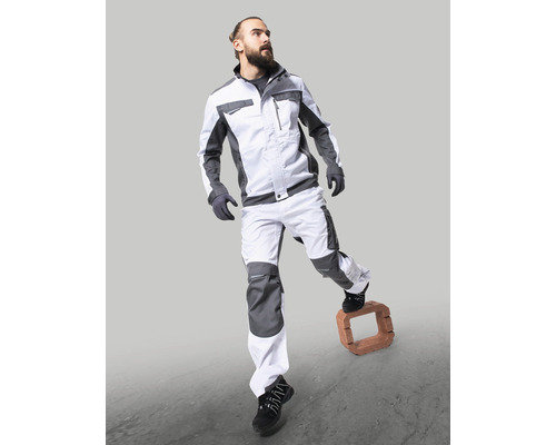 Muž v pracovnom odeve s bundou a nohavicami stojaci na tehle