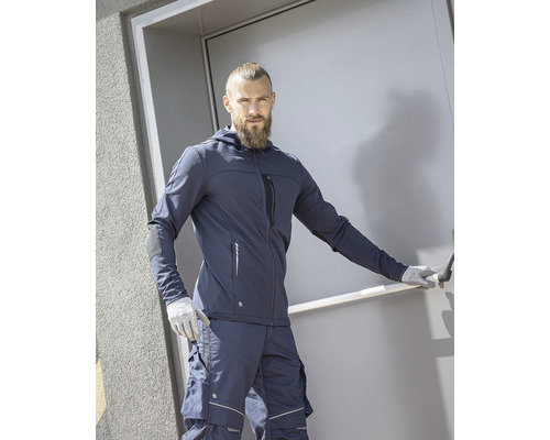 Muž v pracovnom odeve s bundou s kapucňou a pracovnými nohavicami pred dverami