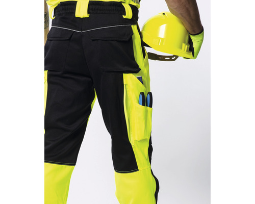 Žlto-čierne pracovné nohavice s vreckami a osoba držiaca ochrannú prilbu