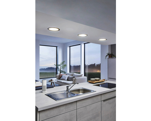 Svetlá kuchyňa so zapustenými bodovými svetlami v strope, drezom a obývacím priestorom v pozadí.