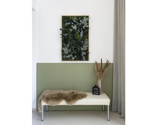 Dekoratívny machový obraz s rôznymi druhmi rastlín, vrátane papradí a eukalyptu, na stene nad lavicou s ovčou kožou