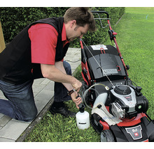 Muž dopĺňa olej do kosačky na trávu