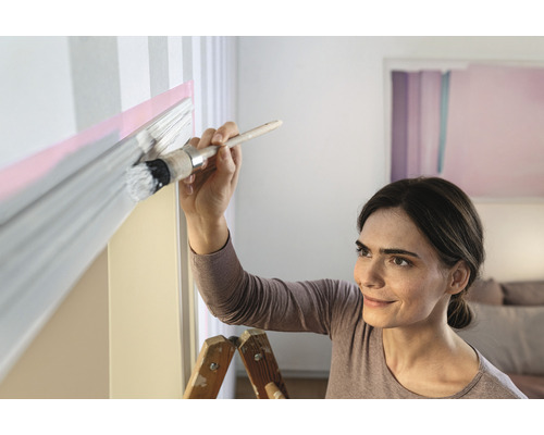 Žena maľuje stenu štetcom a farbou.