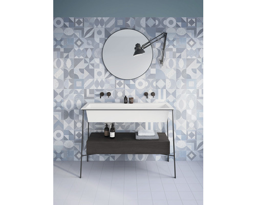 Svetlá kúpeľňa so vzorovanými obkladmi, umývadlo so skrinkou, zrkadlo a lampa.