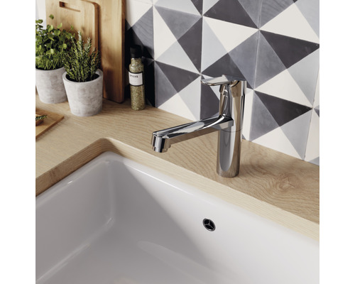 Kuchynská vodovodná batéria z kovu na dreze s pozadím vzorovaných dlaždíc