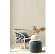 Dekoratívny interiér s ratanovým kreslom, vankúšom a odkladacím stolíkom pred béžovou tapetou.