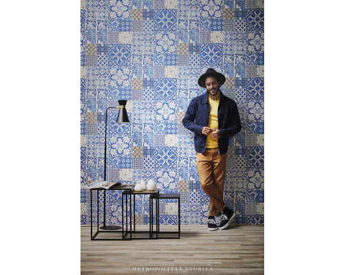 Scéna s nástennou tapetou v patchworkovom dizajne, súpravou príručných stolíkov a stojacou lampou.