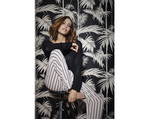 Žena sedí pred tmavou tapetou s rastlinnými motívmi