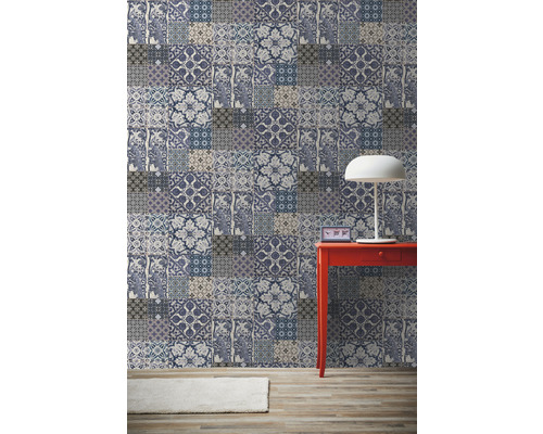 Pohľad do miestnosti s patchworkovou tapetou, červeným stolom a lampou