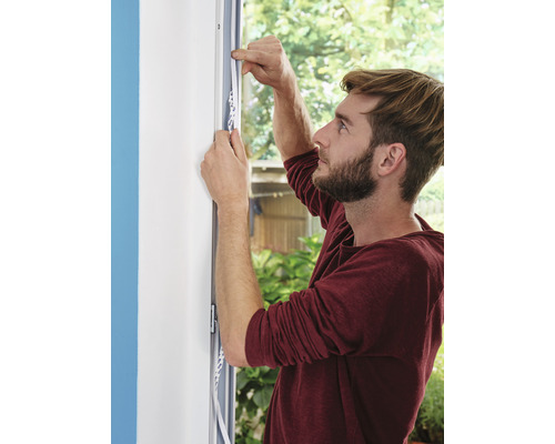 Muž pripevňuje tesniacu pásku na rám okna.