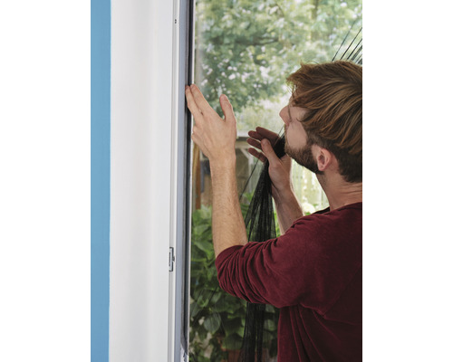 Muž pripevňuje sieť proti hmyzu na okenný rám.