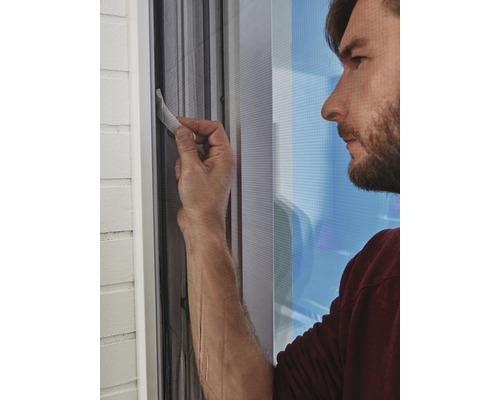 Muž montuje sieť proti hmyzu na okno