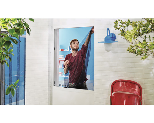 Muž pripevňuje na okno sieť proti hmyzu, aby sa zabránilo vniknutiu hmyzu