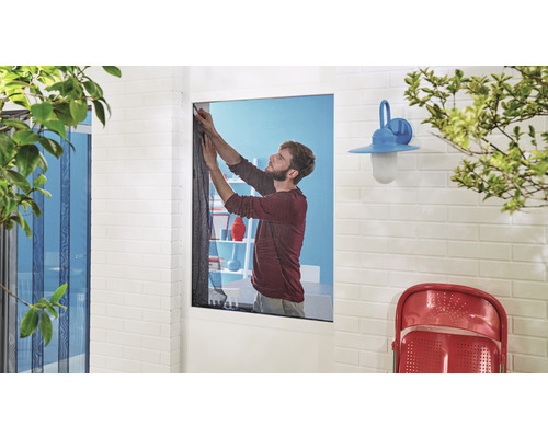 Muž montuje sieť proti hmyzu na okno domu s tehlovou stenou a vonkajším osvetlením