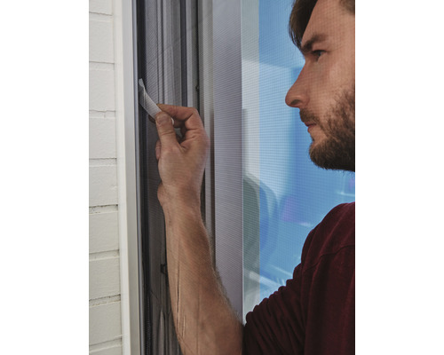 Muž upevňuje sieť proti hmyzu na okenný rám