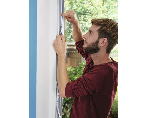 Muž upevňuje tesniacu pásku na okenný rám.