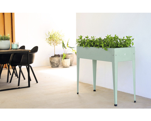 Scéna s vyvýšeným záhonom z kovu, osadeným zelenými rastlinami, a tiež rastlinami v kvetináčoch a stolom so stoličkami