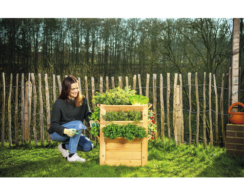 Žena pracuje na drevenom trojposchodovom bylinkovom záhone v záhrade