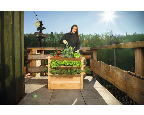 Žena záhradničí vo vyvýšenom záhone na balkóne s dreveným plotom.