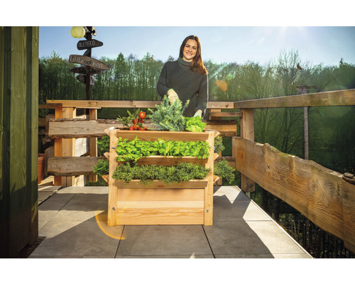 Žena s dreveným hrantíkom s tromi úrovňami a rôznou zeleninou na balkóne.