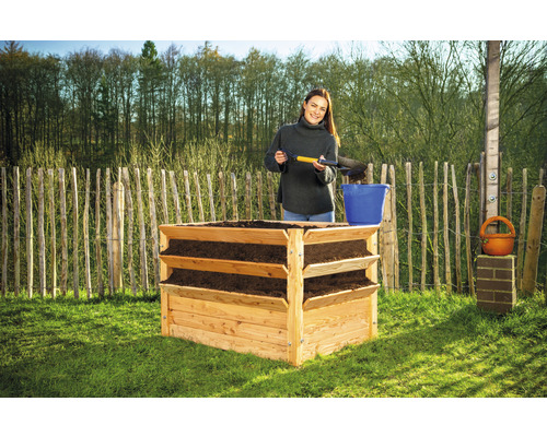 Drevený vyvýšený záhon s tromi úrovňami a ženou, ktorá pridáva zeminu.