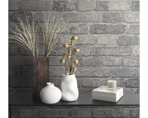 Dekoratívna scéna s vázami, rastlinami, sviečkou a stohom kníh proti kamennej stene.