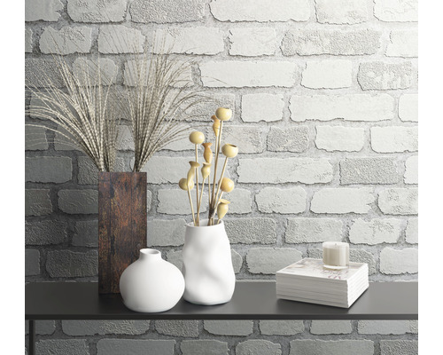 Dekoratívne usporiadanie zátišia s vázami, rastlinami a knihami na pozadí tehlovej steny.