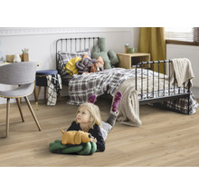 Dieťa leží na laminátovej podlahe v detskej izbe s posteľou a písacím stolom