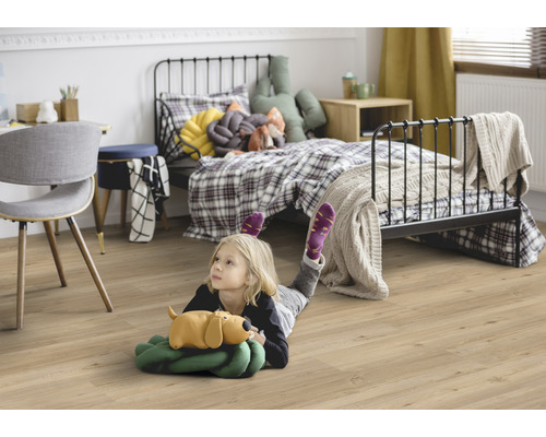 Dieťa leží na laminátovej podlahe v detskej izbe s posteľou a písacím stolom