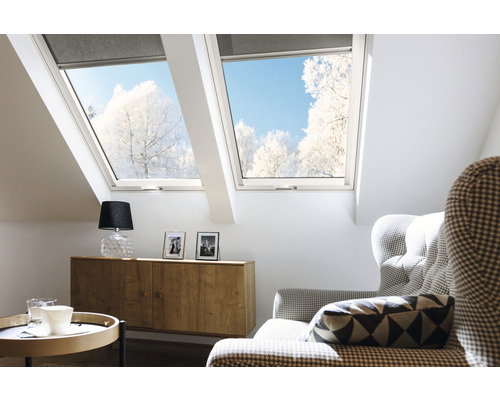 Svetlá podkrovná izba so strešnými oknami a roletami, zariadená komodou, lampou a kreslom