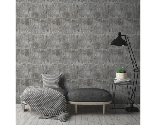 Sivá tehlová tapeta v štýlovom obývacom prostredí s lampou, taburetom a vankúšmi.