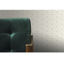 Detail geometrickej tapety so zeleným kreslom v popredí.