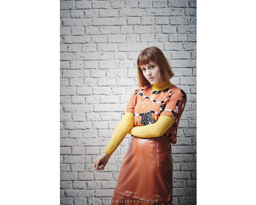 Žena s tričkom so vzorom a lesklou sukňou pred tehlovou stenou