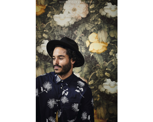 Muž s klobúkom pred kvetinovou tapetou z kolekcie Metropolitan Stories.