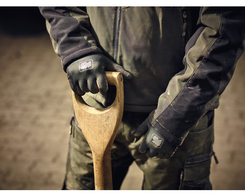 Osoba v pracovnom odeve drží rýľ s drevenou rukoväťou a má na sebe pracovné rukavice.
