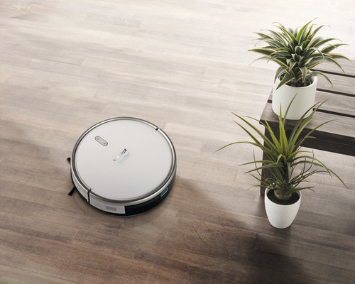 Robotický vysávač na drevenej podlahe vedľa hrnkových rastlín na lavici